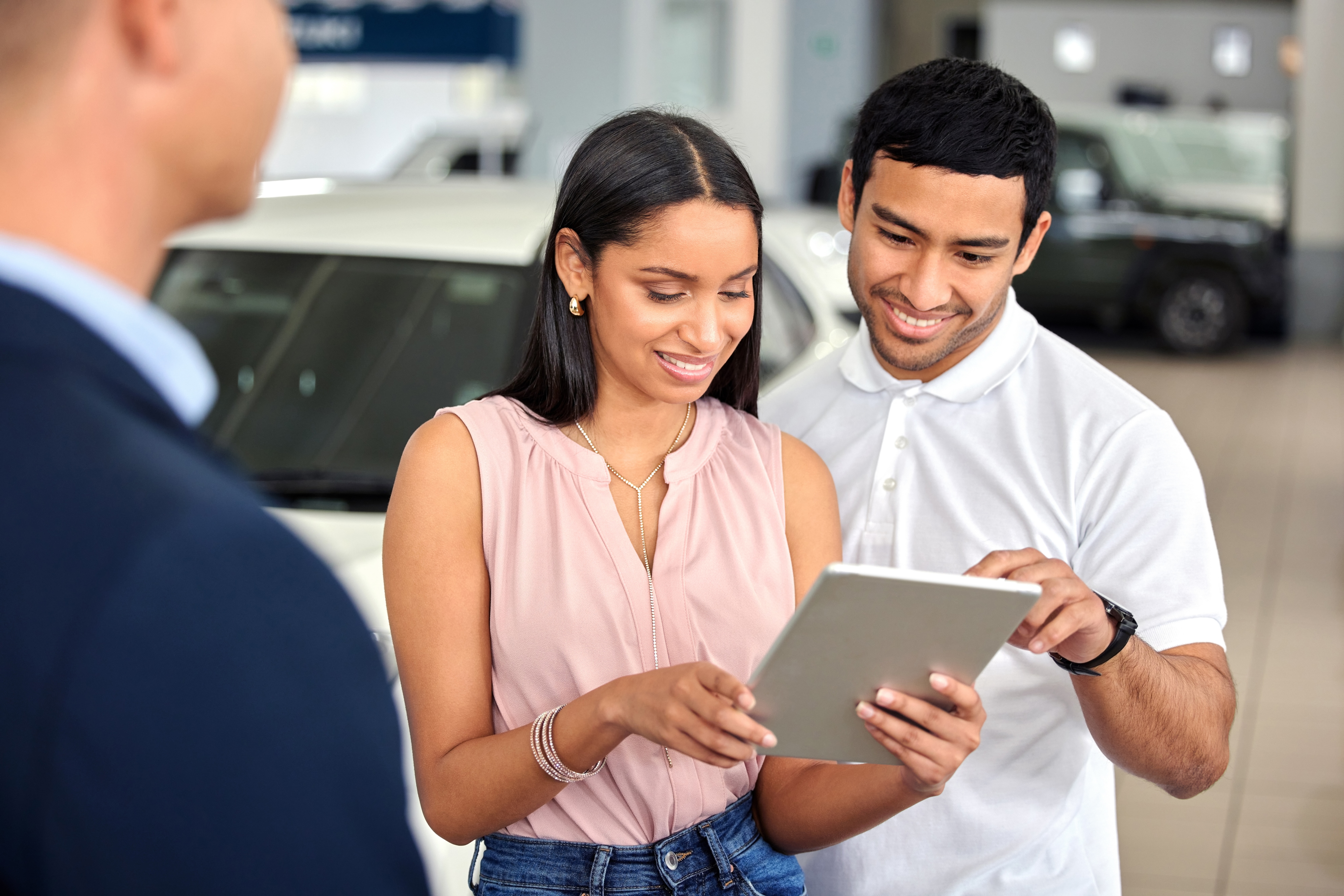 A smiling couple at an automotive dealership using a tablet to explore options, illustrating the importance of employee experience in dealerships. This interaction emphasizes how a positive employee experience enhances customer experience, driving trust and loyalty in automotive dealerships.