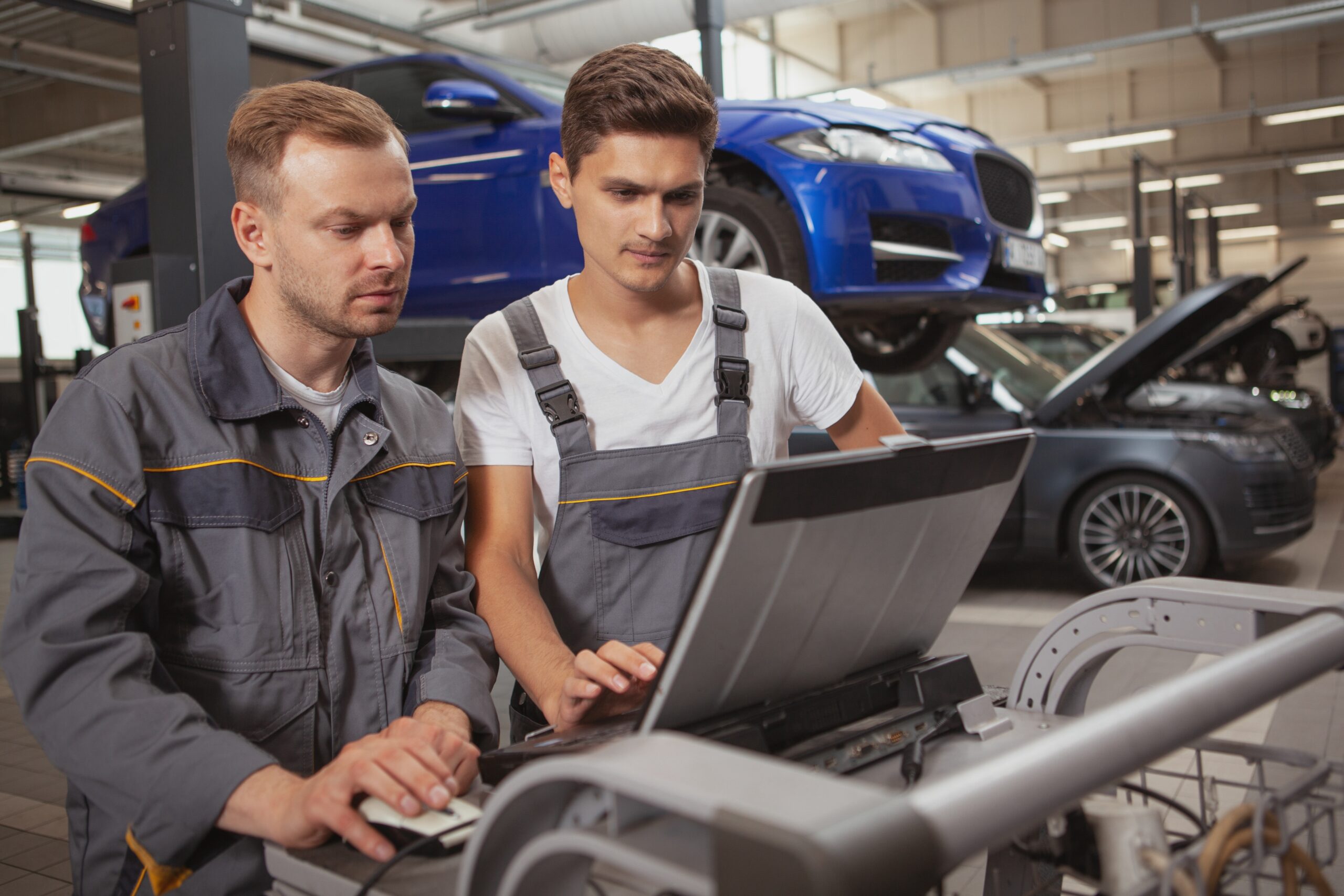 Two automotive technicians in a dealership service area using a computer to enhance customer experience, illustrating how better employee experience drives customer trust and loyalty